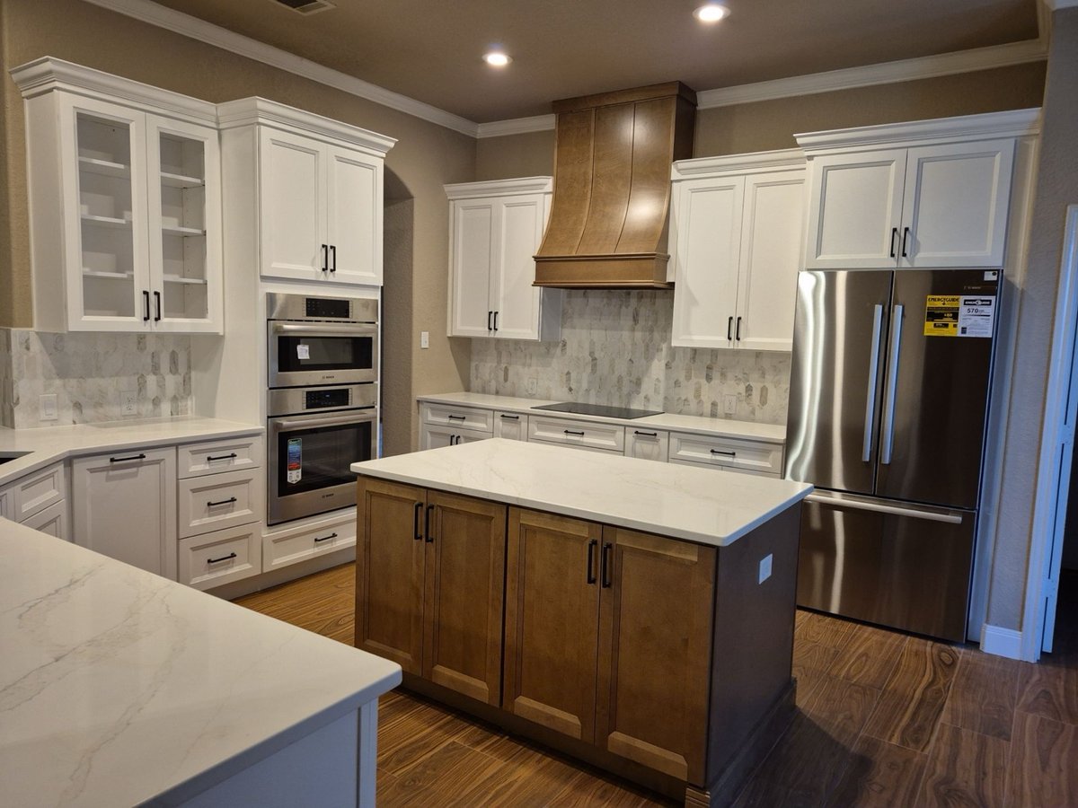 White kitchen with wood range hood, marble counters, and stainless refrigerator