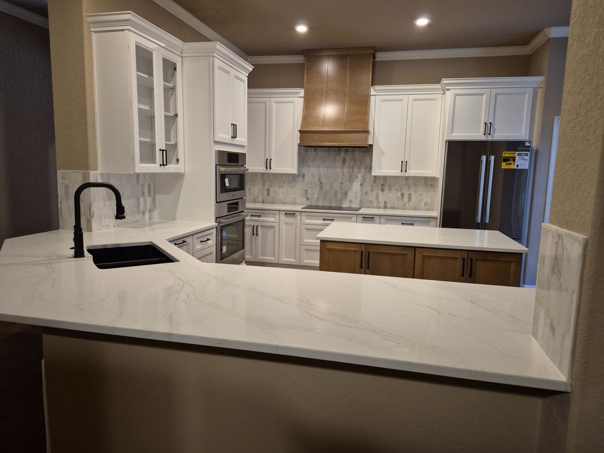 Open kitchen with marble peninsula, white cabinets, and stained wood island