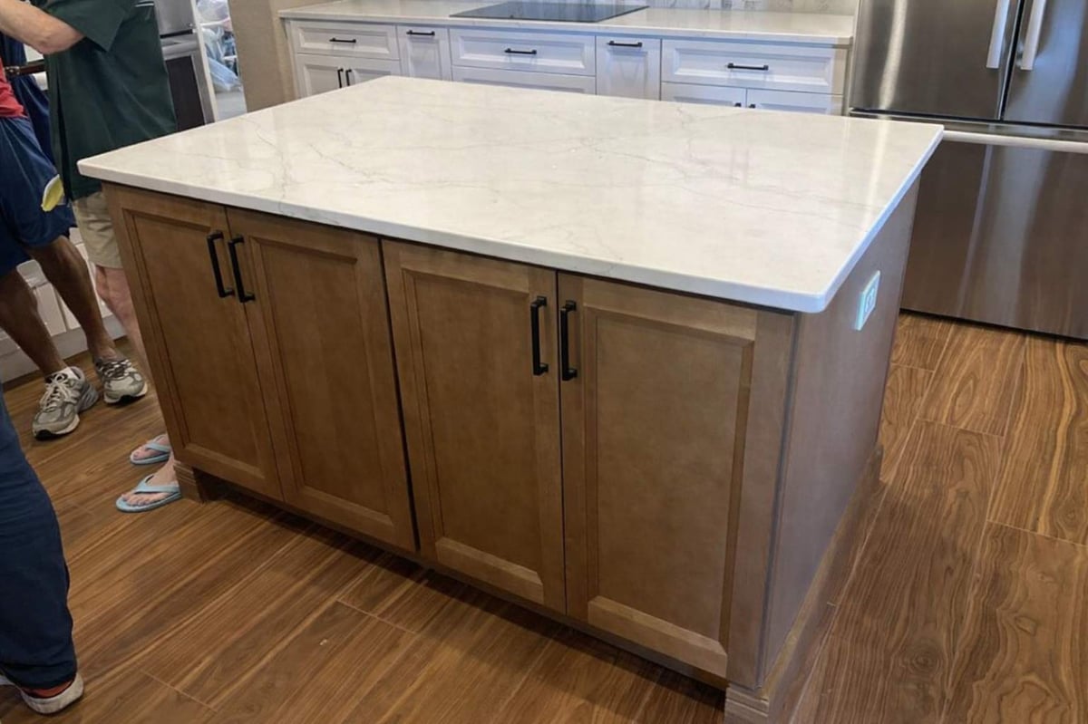 Stained wood kitchen island topped with white marble and black cabinet pulls