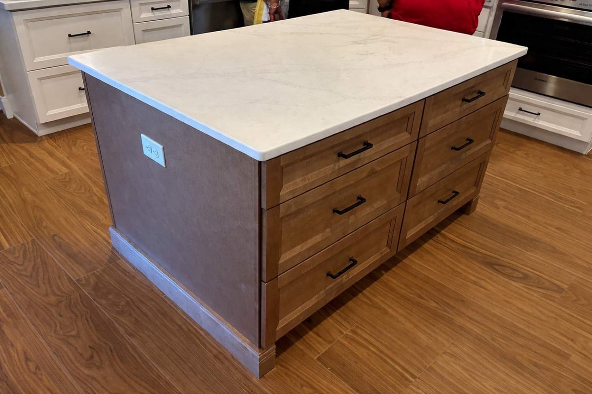 Two-tone wood island with marble top set on plank flooring in white kitchen