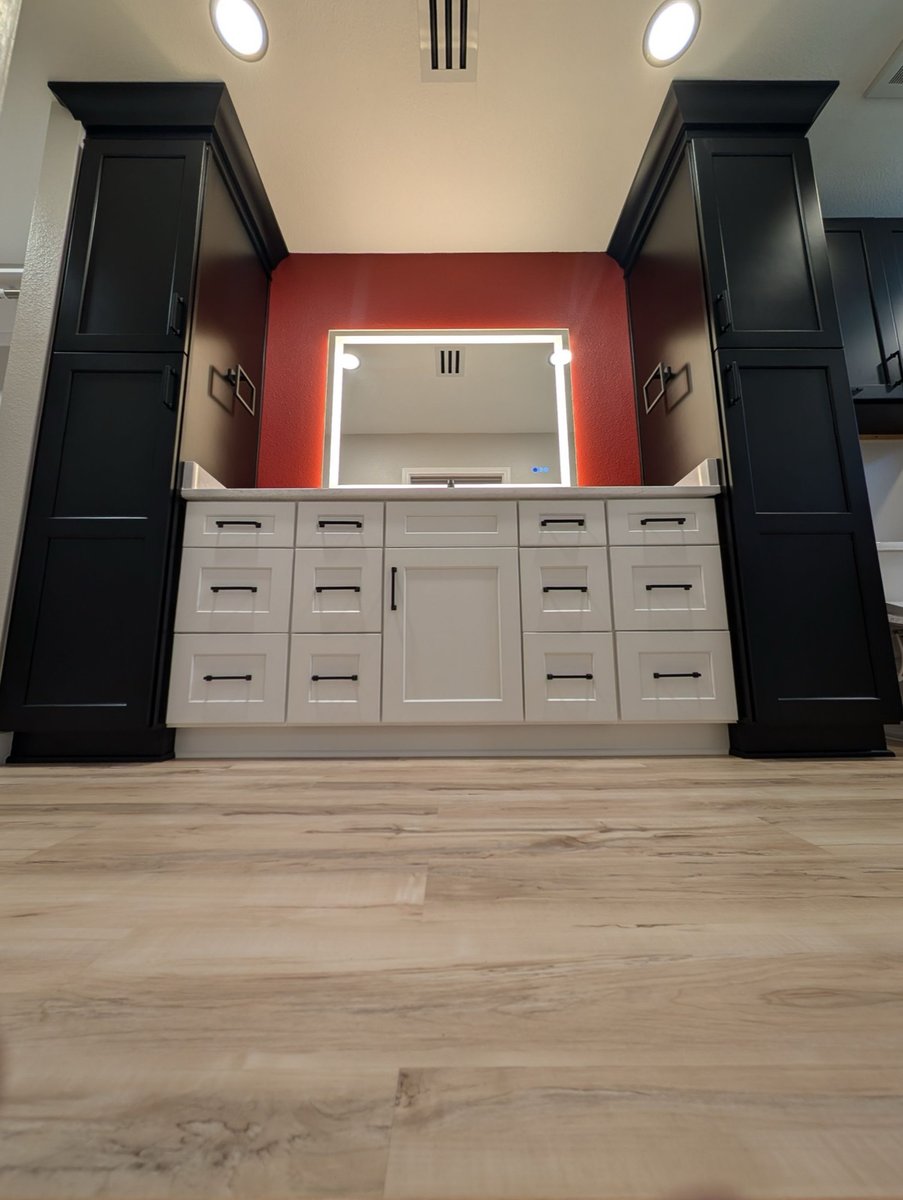 White vanity flanked by tall black cabinets with lit mirror on red accent wall