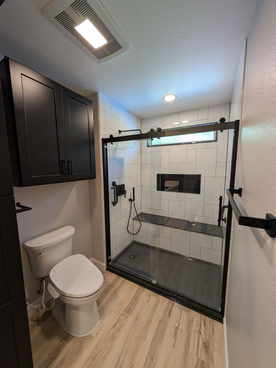 Walk-in shower with white subway tile, black bench, sliding glass door, and toilet