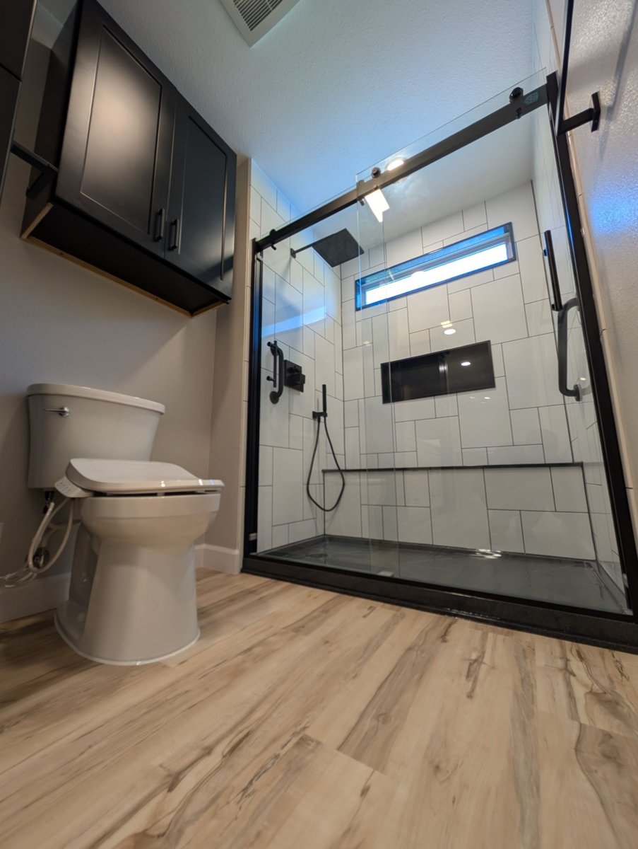 White subway tile walk-in shower with black rainfall head, bench, and toilet