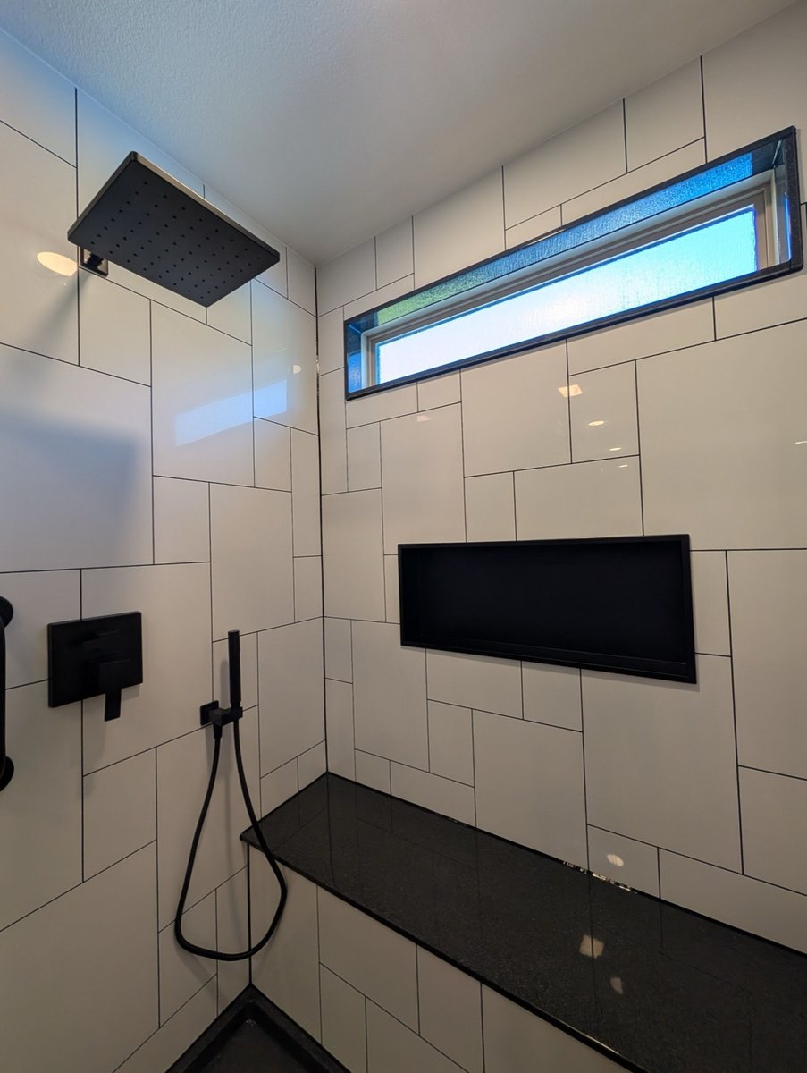 Black rainfall showerhead and handheld on white subway tile above black bench
