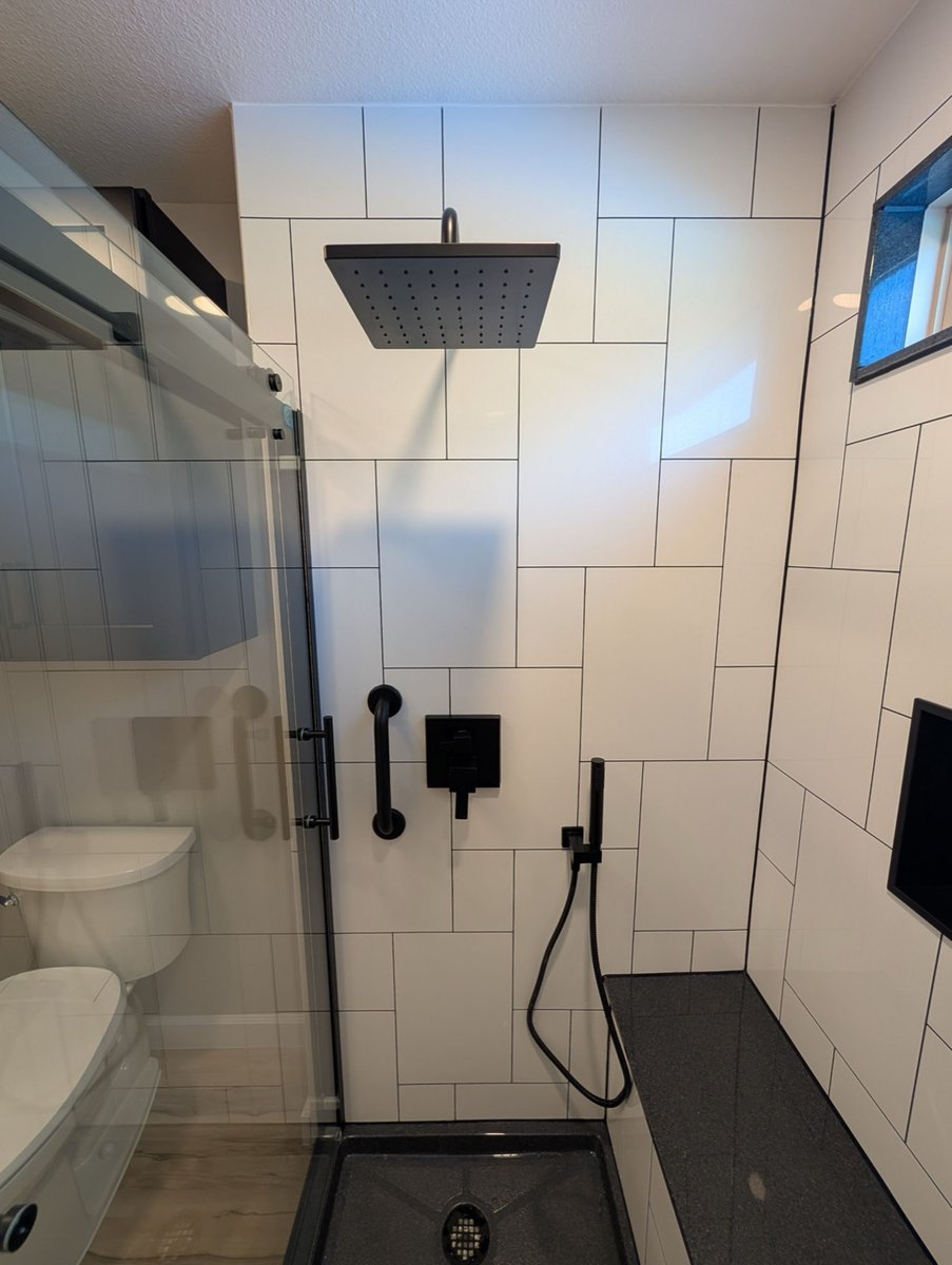 Black square rainfall showerhead and grab bar in white subway tile shower