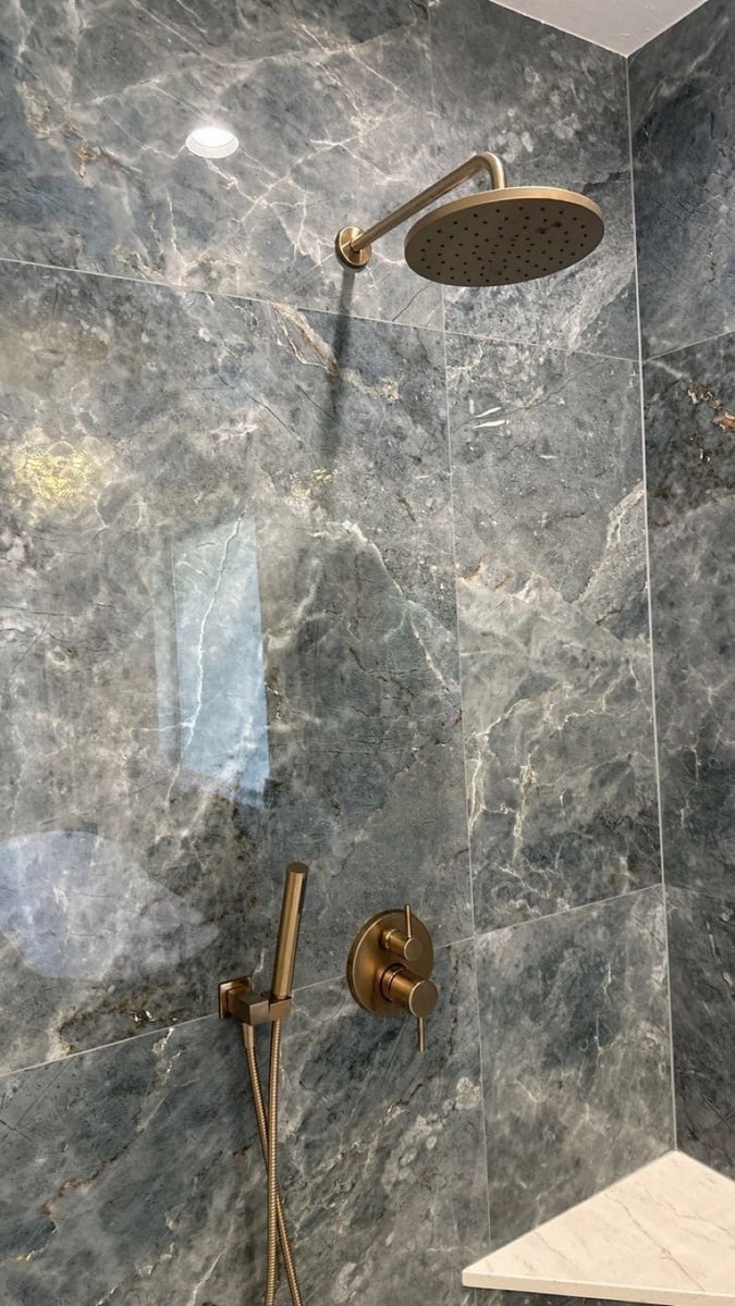 Walk-in shower with dark marble walls, gold rainfall head, and gold fixtures