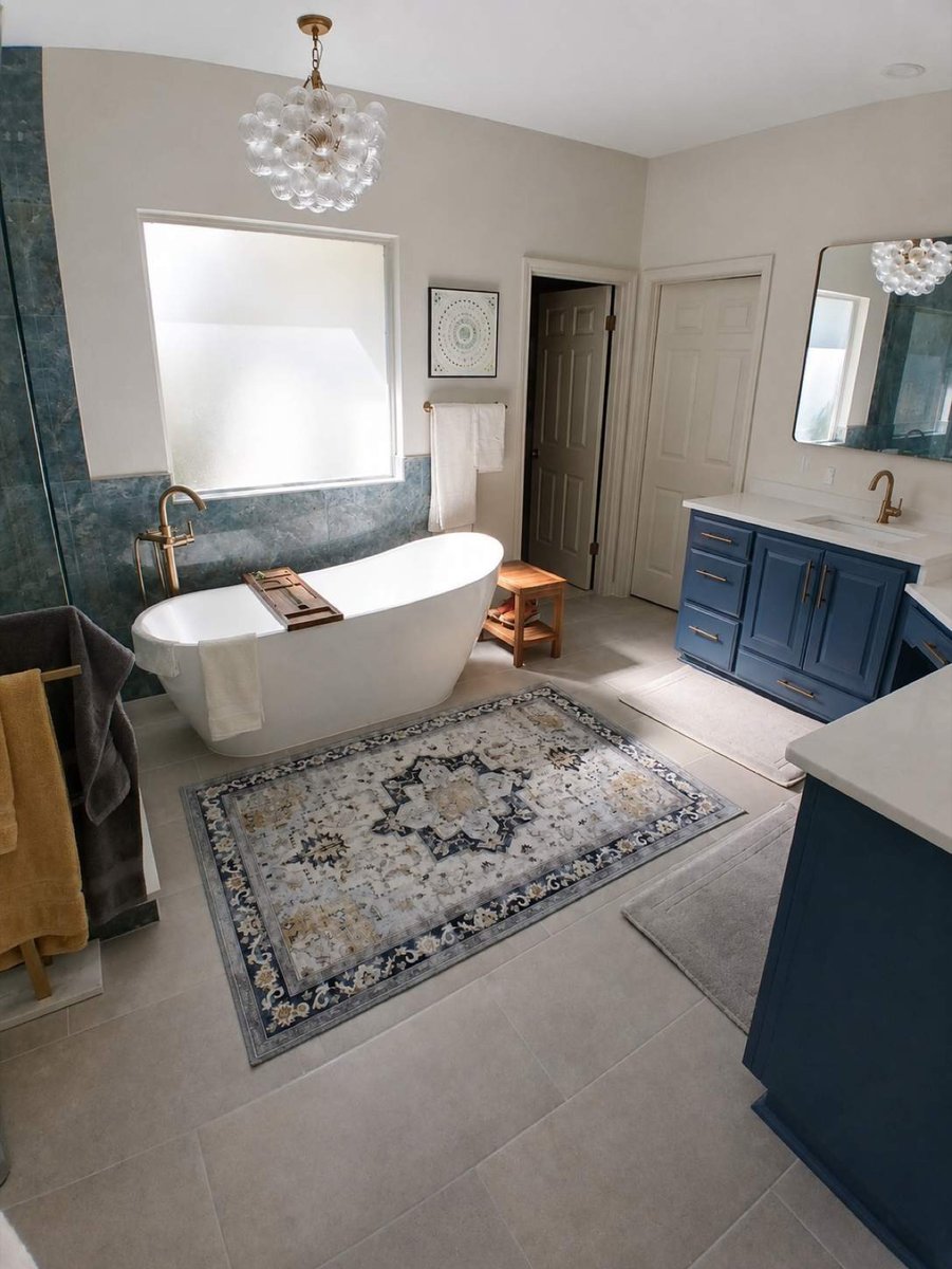 Soaking tub and navy vanity with gold fixtures, area rug, and bubble chandelier