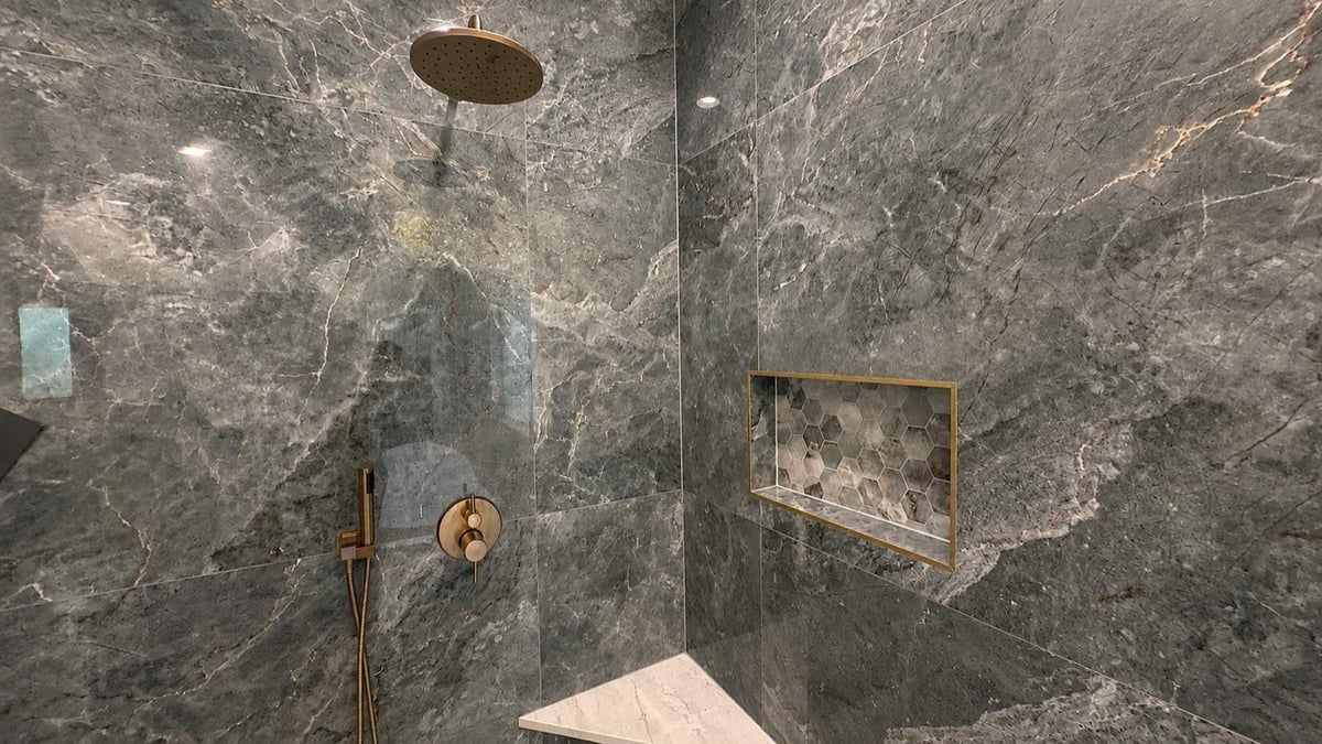 Dark marble shower with gold rainfall head and hexagon mosaic accent niche