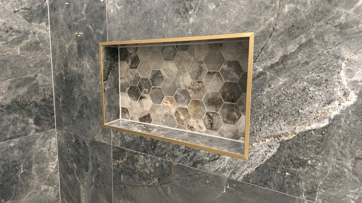 Gold-framed hexagon mosaic shower niche set into dark gray marble tile