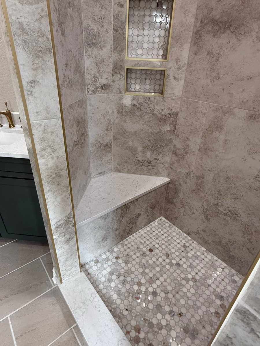Shower corner with gray marble tile, penny mosaic floor and bench beside green vanity