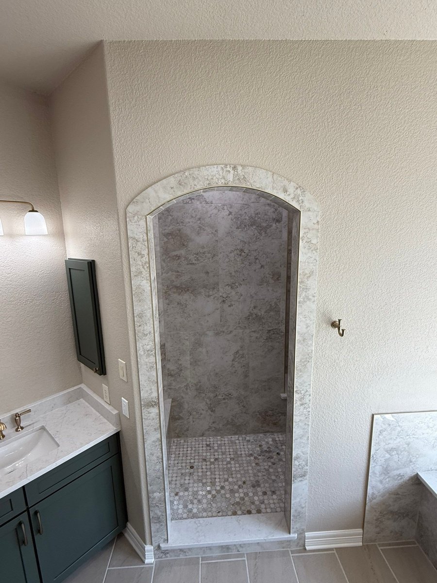Arched walk-in shower alcove with gray marble tile beside green vanity