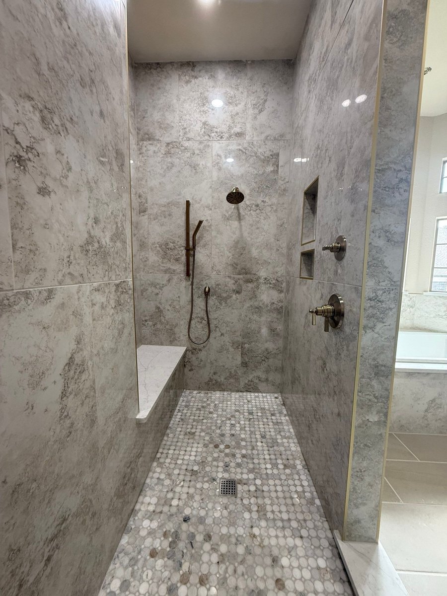 Walk-in shower with gray marble walls, brushed nickel fixtures and pebble floor