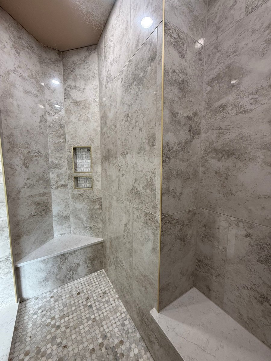 Gray marble shower interior with corner bench, niche and penny tile floor