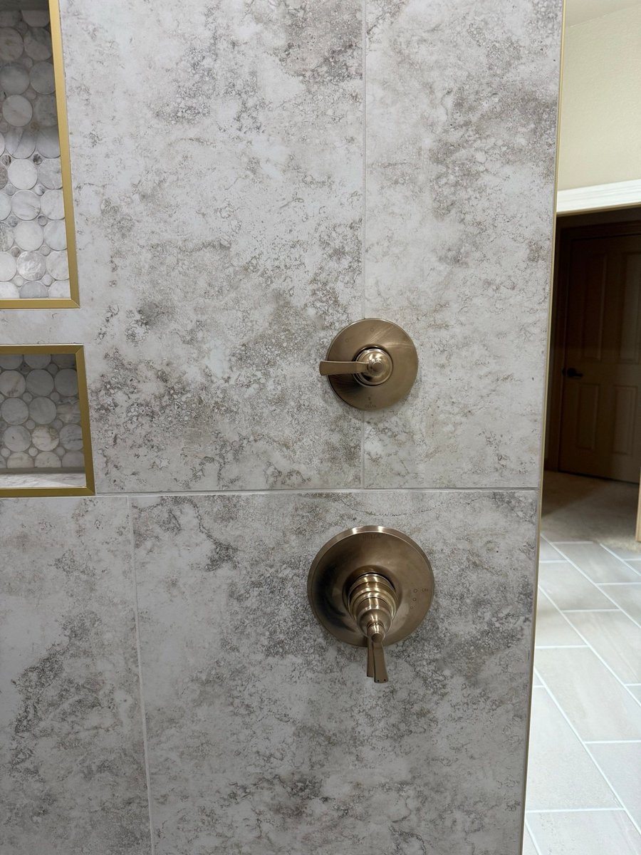 Close-up of brushed gold shower valve and lever on gray marble tile