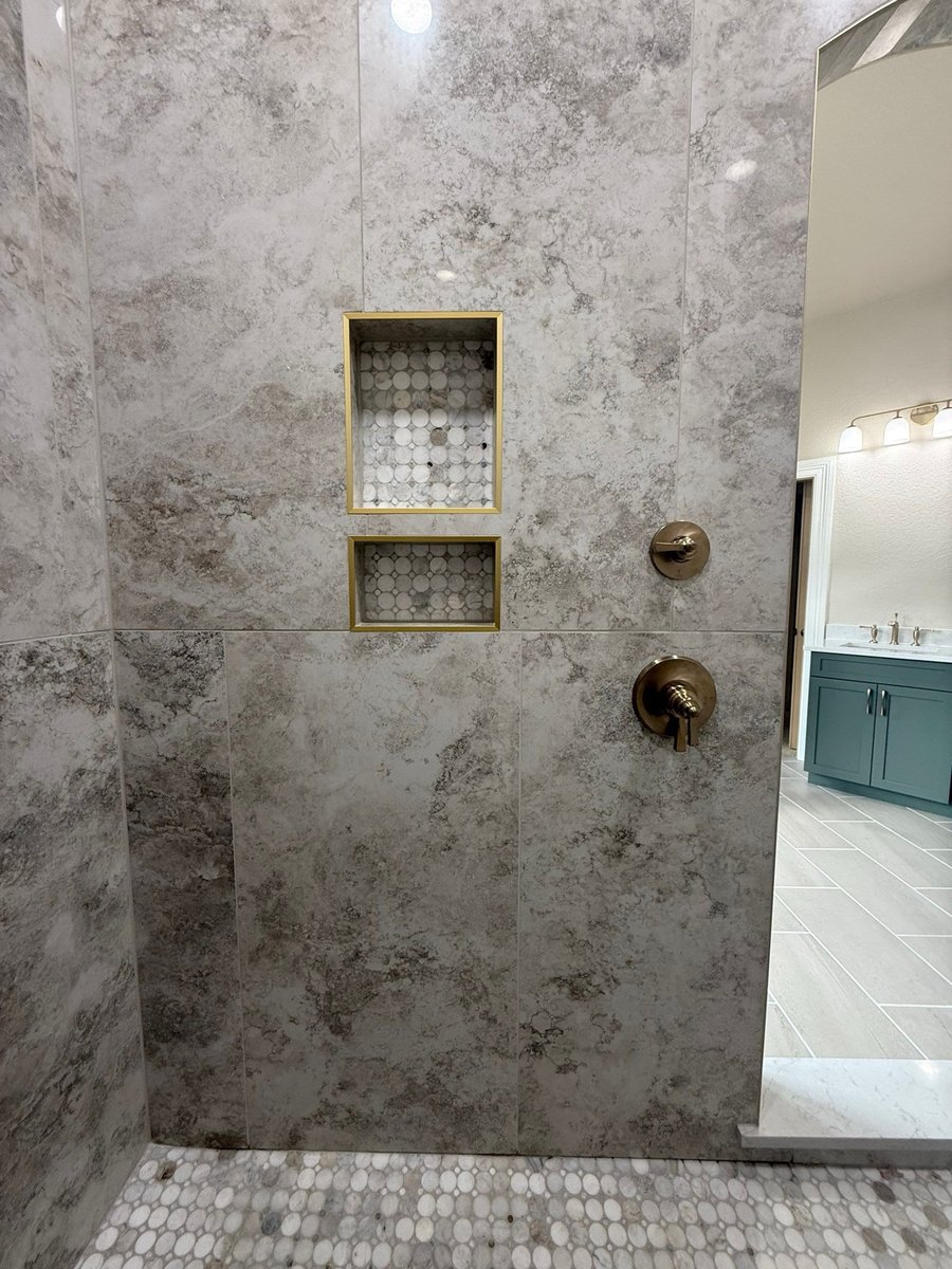 Gray marble shower wall with recessed niches and gold trim beside vanity view
