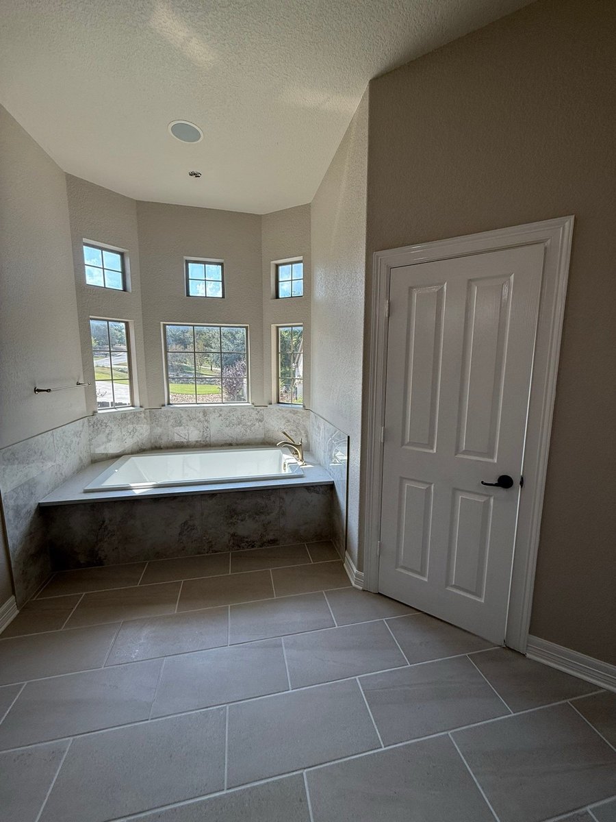 Original drop-in tub under bay windows with gray tile surround and white door