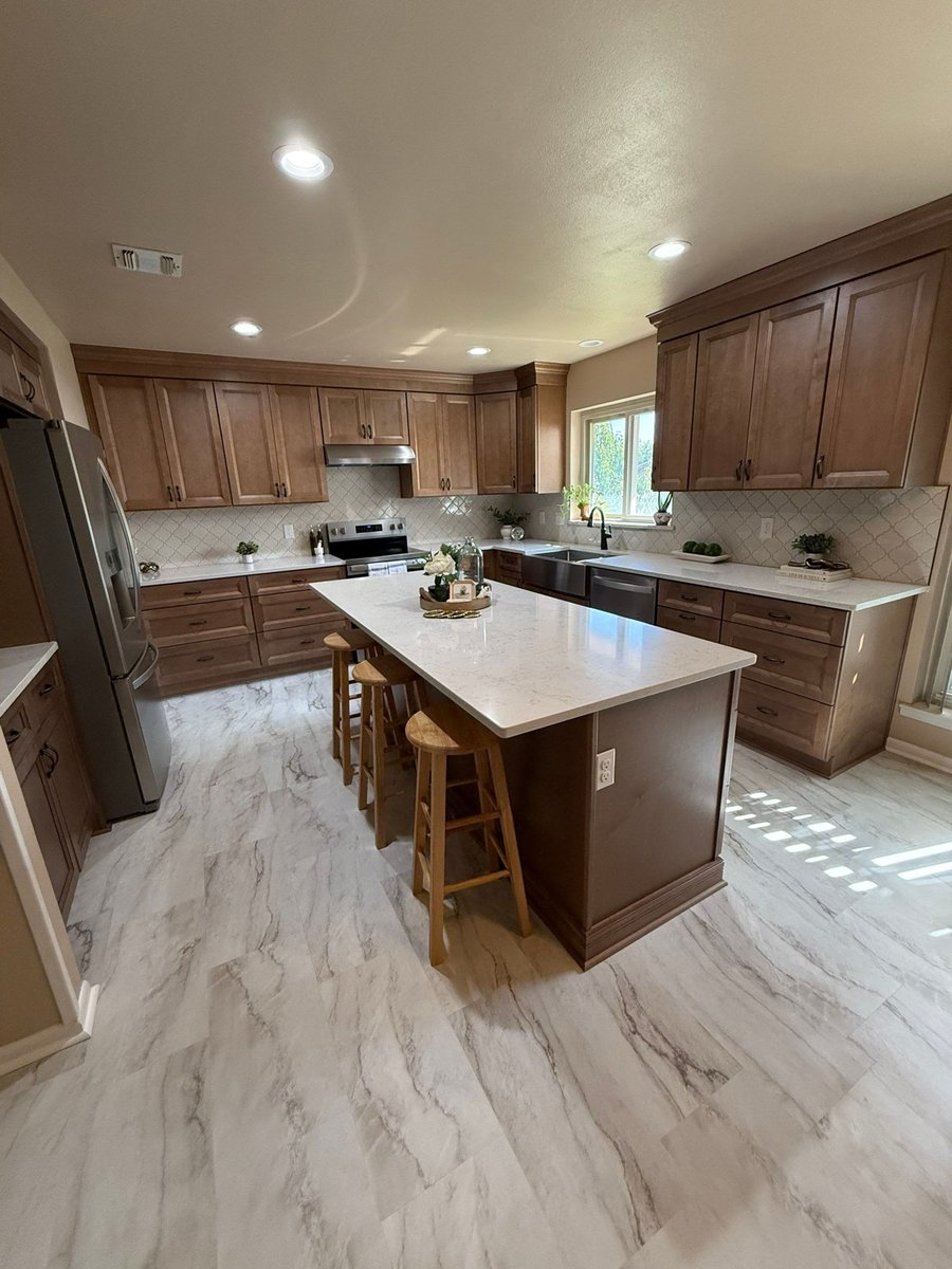 Wide view of wood cabinet kitchen with quartz island and marble-look tile floor