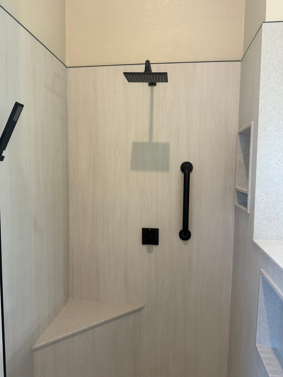 Wood-look shower walls with black rainfall fixture, grab bar and corner bench