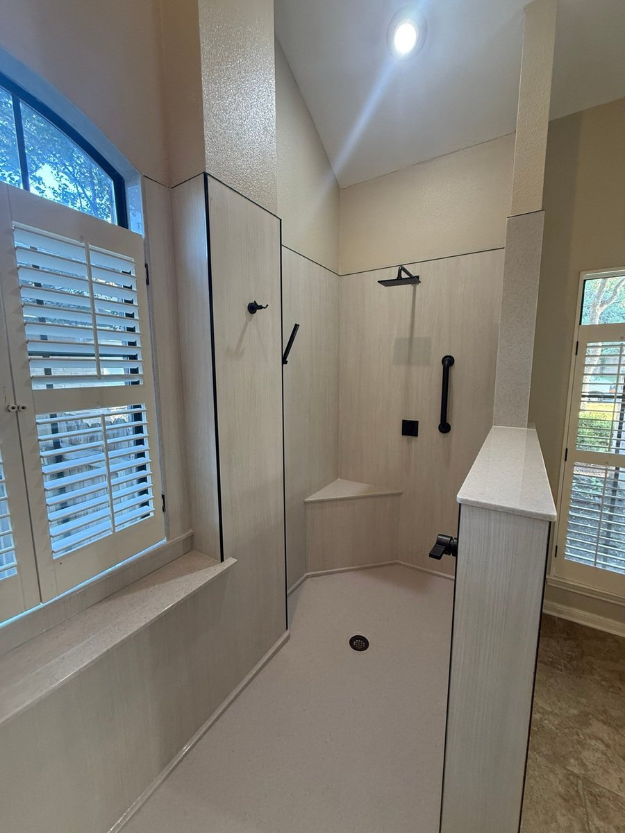 Accessible roll-in shower with wood-grain walls, black fixtures and plantation shutters