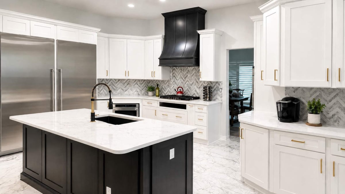 White kitchen with dark island, stainless refrigerator, black hood, and gold pull-down faucet