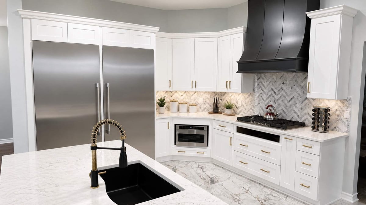 White kitchen with black island sink, large stainless refrigerator, and black range hood