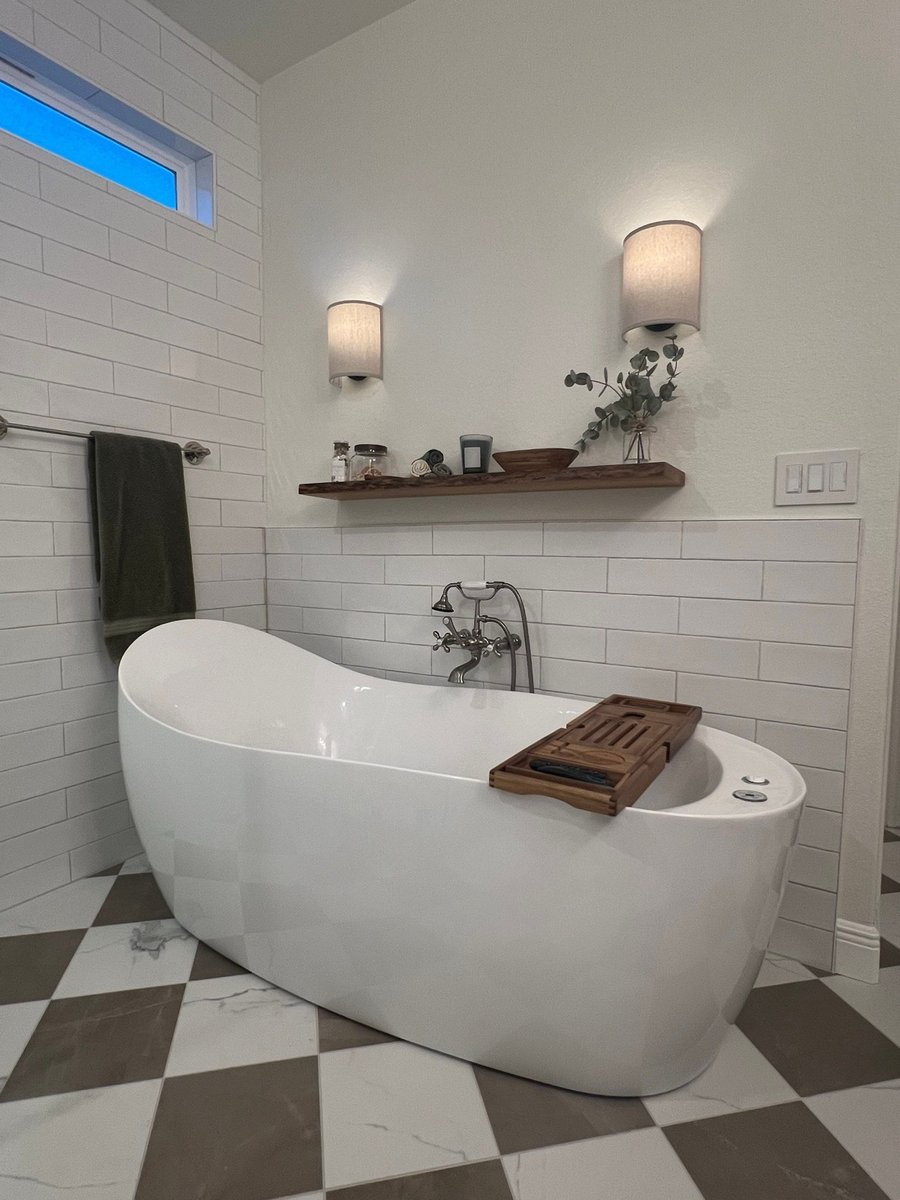 Freestanding tub against white subway tile with wood bath caddy and sconces