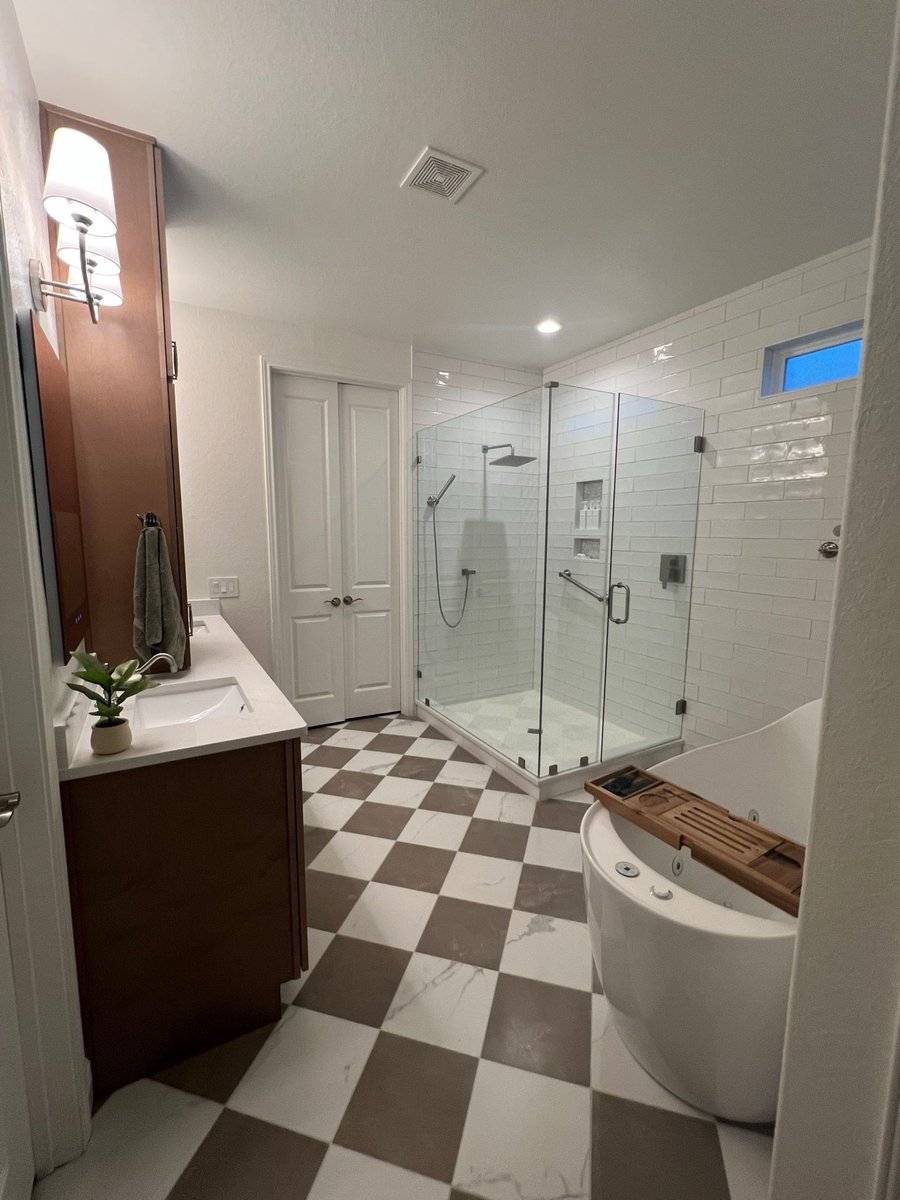 Corner glass shower and freestanding tub over checkered marble flooring