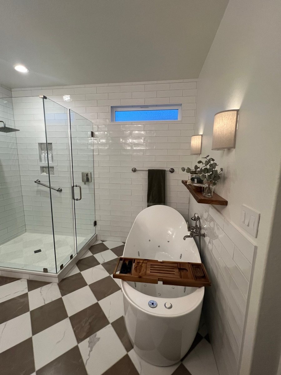 White tiled walk-in shower beside an oval soaking tub and checkered floor