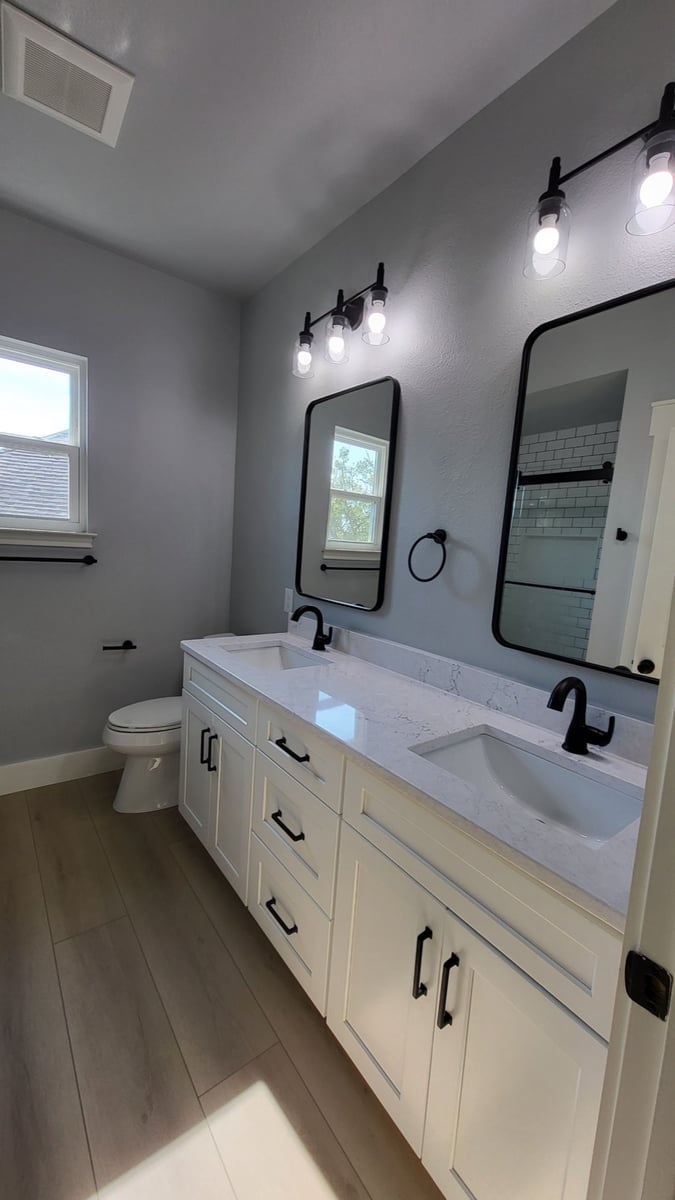 Bright bathroom with gray walls, black mirrors, white vanity and dual sinks