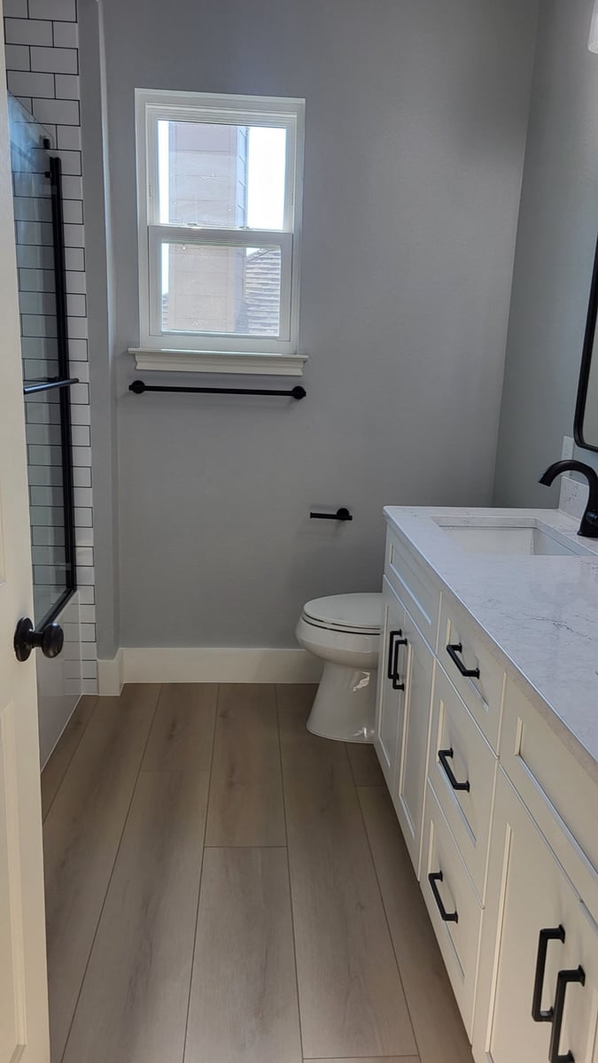 Bathroom with white vanity, subway-tiled tub-shower and black hardware