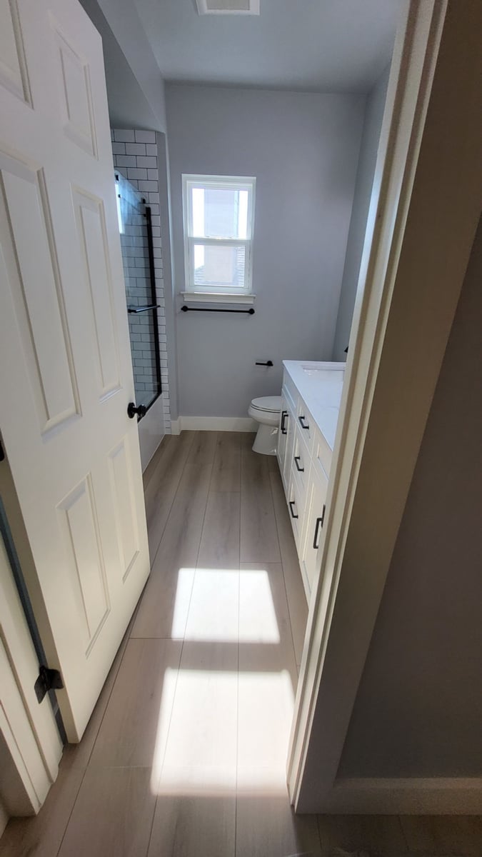 Narrow bathroom with subway-tiled tub, white vanity and wood-look floor