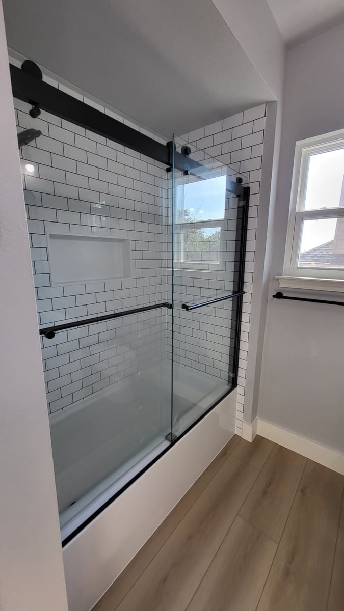Tub-shower with white subway tile, black framed sliding door and grab bar