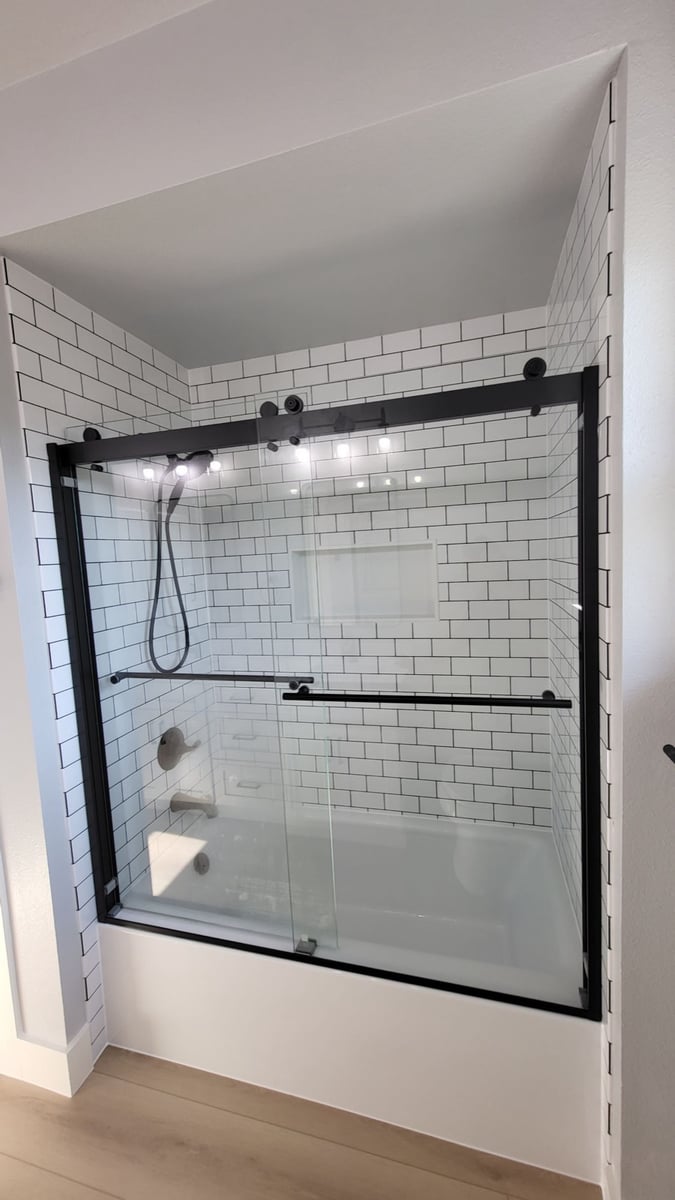 Subway-tiled tub with black-framed glass doors and handheld shower
