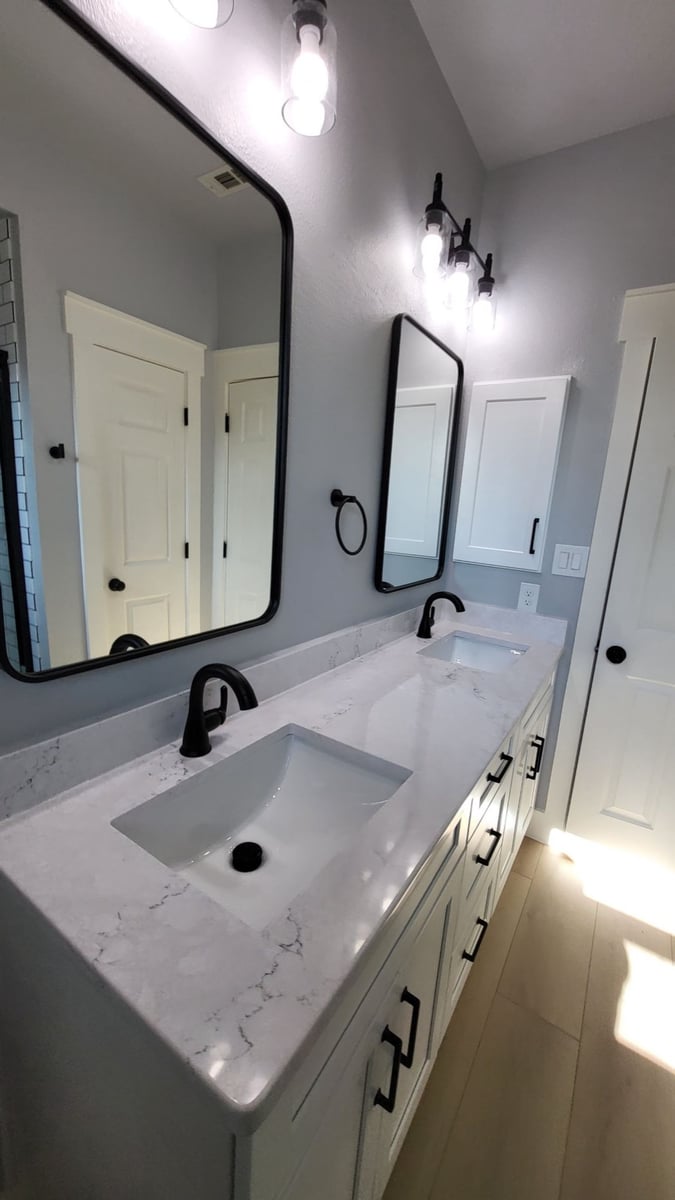 Double white vanity with marble-look quartz, black faucets and framed mirrors