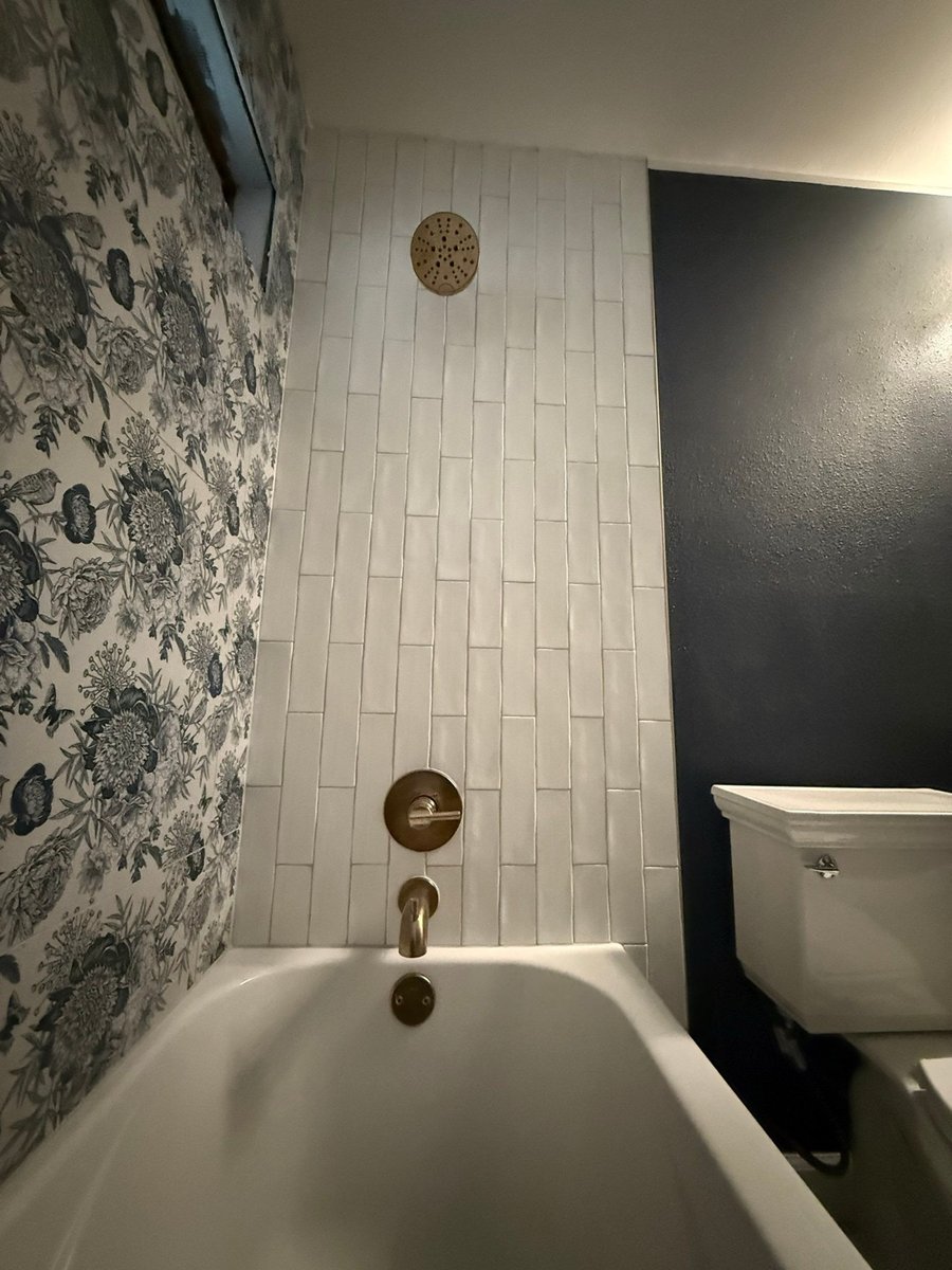 White tub-shower with floral wallpaper accent against navy walls and brass fixtures