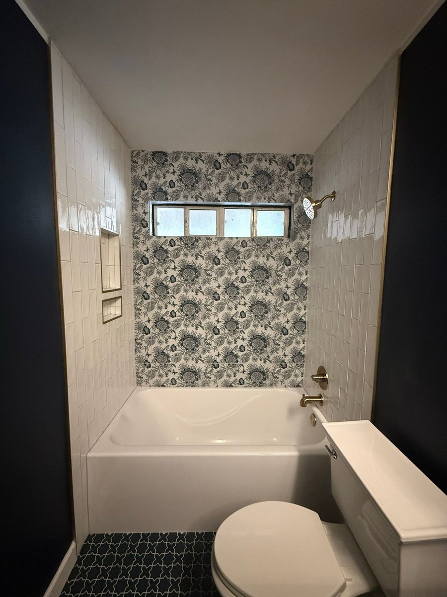 White tub-shower with floral wallpaper, glass-block window and brass head