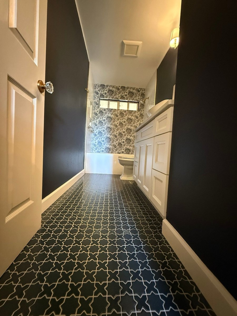 Long view down navy bath to floral-papered tub and white vanity