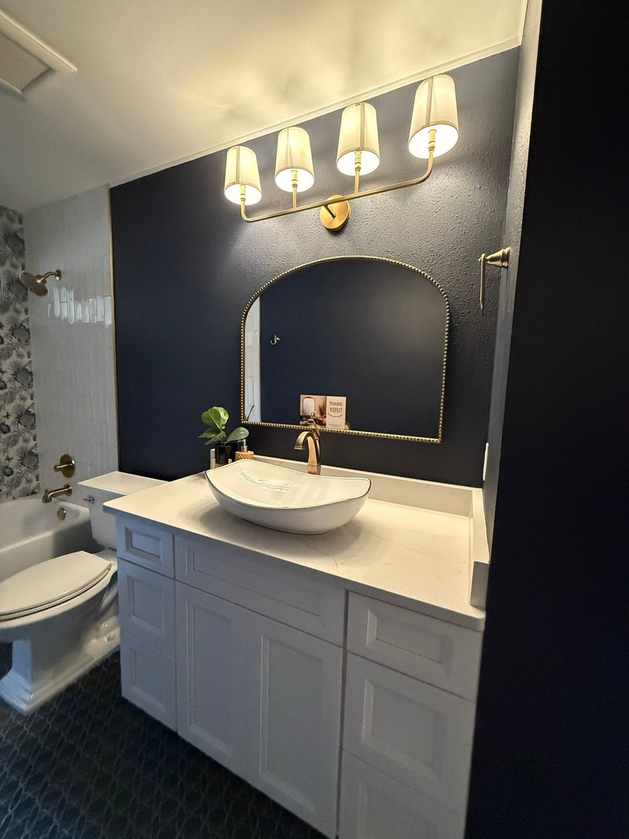 Navy bath with brass sconces, beaded arch mirror and white vessel sink vanity