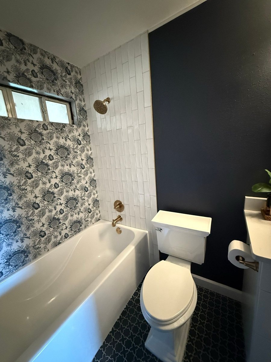 Floral wallpaper tub-shower with brass head beside navy accent wall