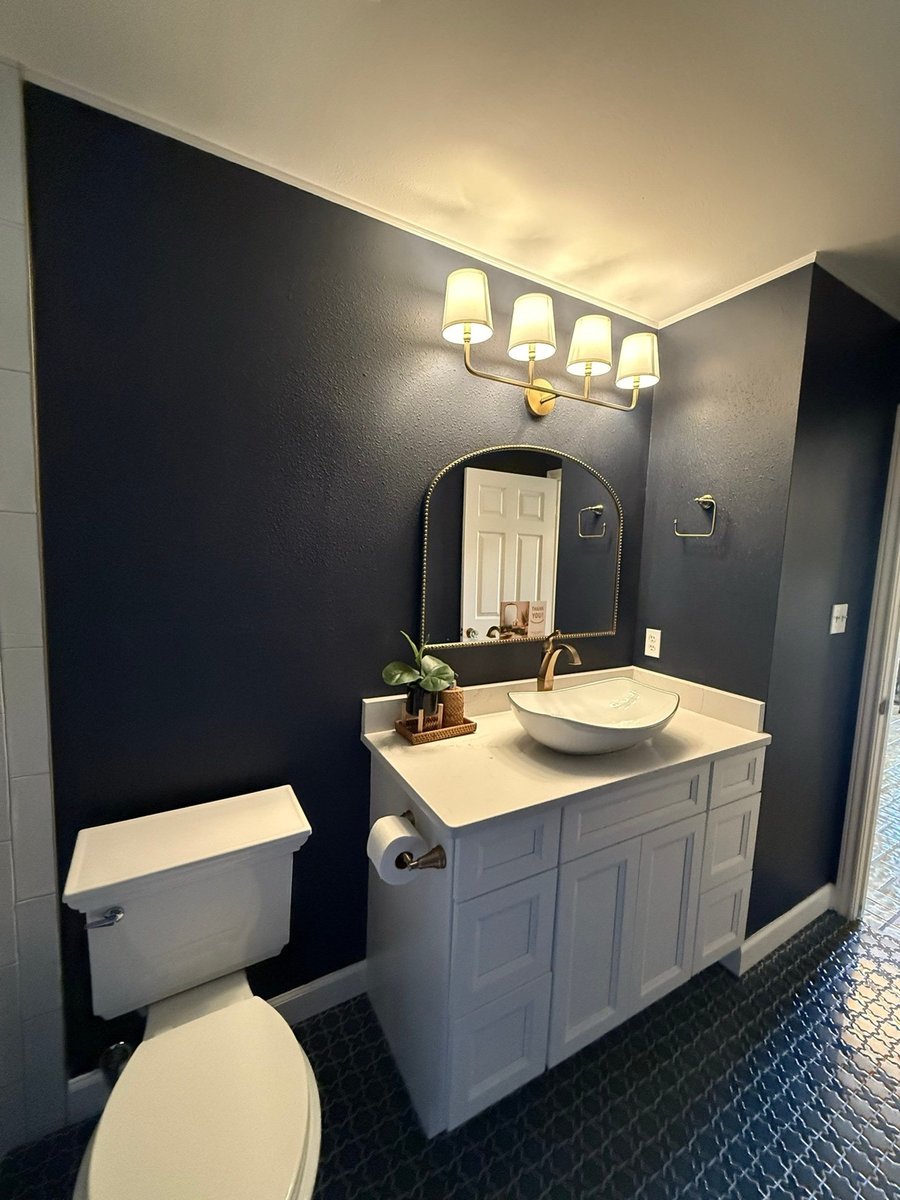 Navy bath with brass sconces, arched mirror and white vessel-sink vanity