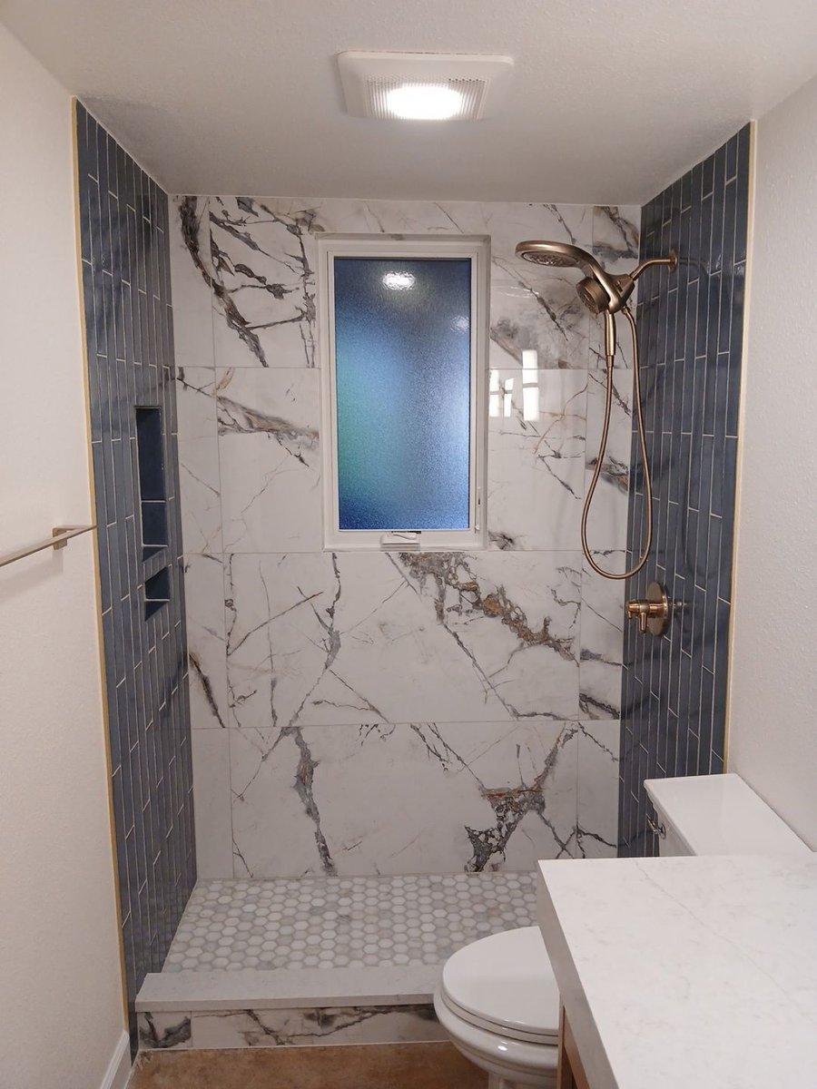 Walk-in shower with white marble walls, vertical blue tile and brushed gold fixtures