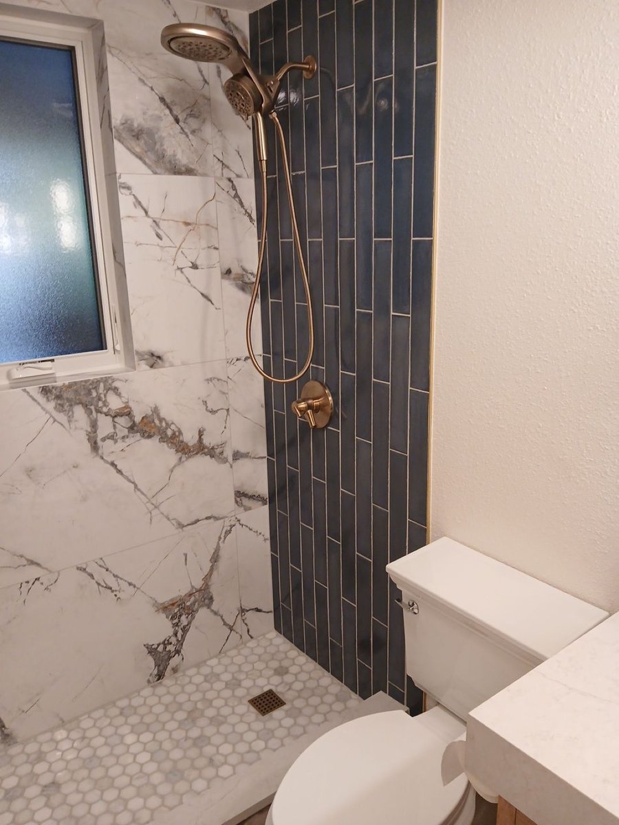 Shower corner with blue tile, hexagon mosaic floor and brass handheld sprayer