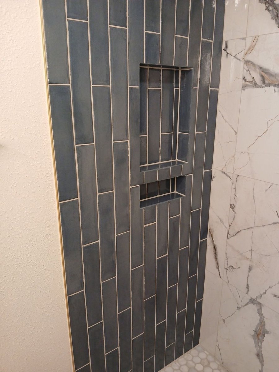 Vertical blue tile shower wall with recessed double niche beside marble tile