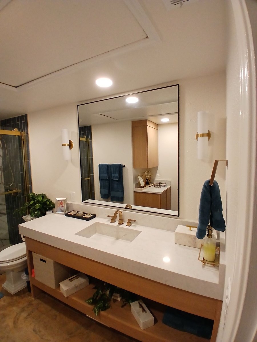 Floating wood vanity with white quartz counter, black framed mirror and blue towels