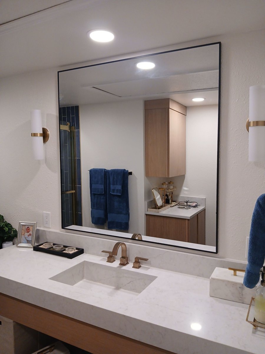 Wide black framed vanity mirror reflecting wood storage cabinet and navy towels