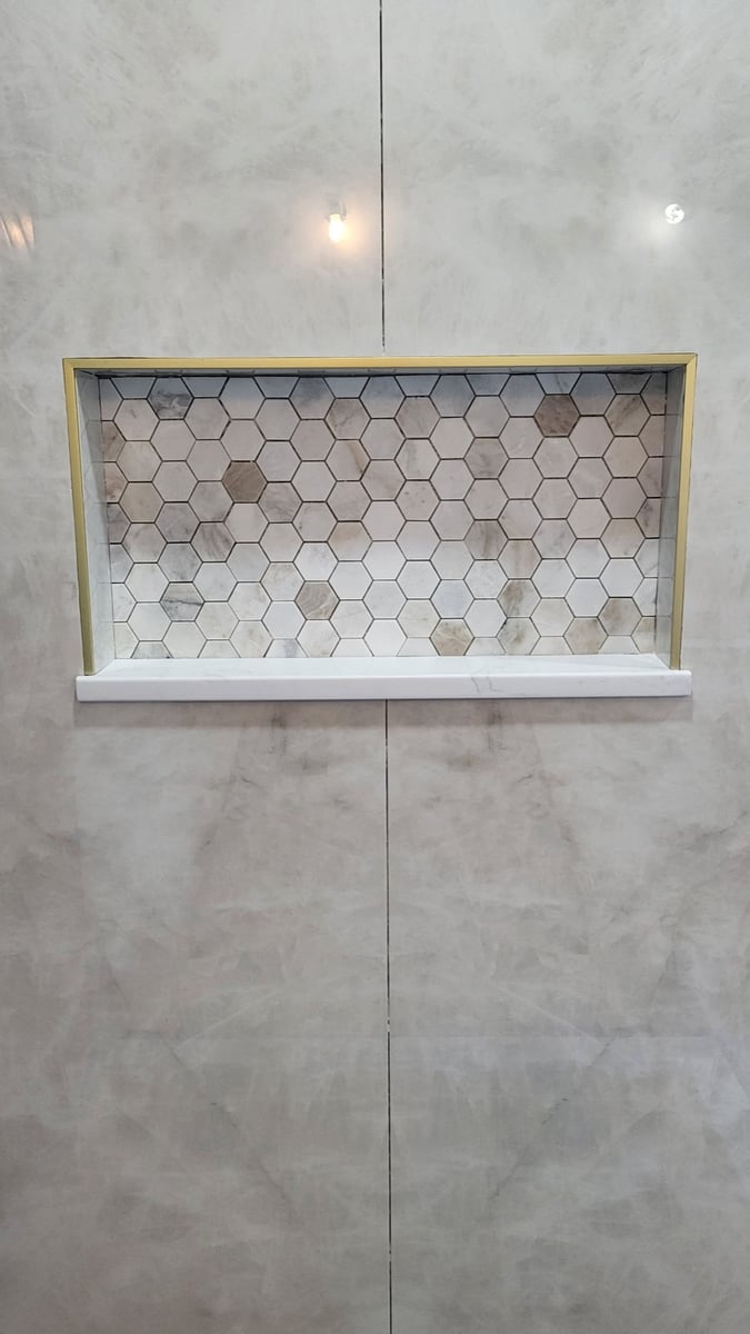 Recessed shower niche with gold trim and marble hexagon mosaic in gray marble wall