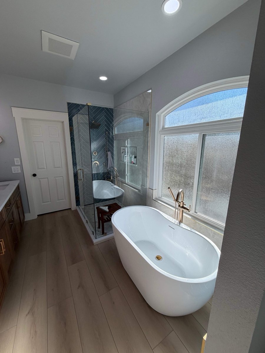 Master bath with freestanding tub by arched window and corner glass shower