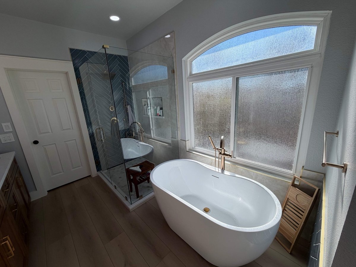 White freestanding tub and corner glass shower with white door and wood floor