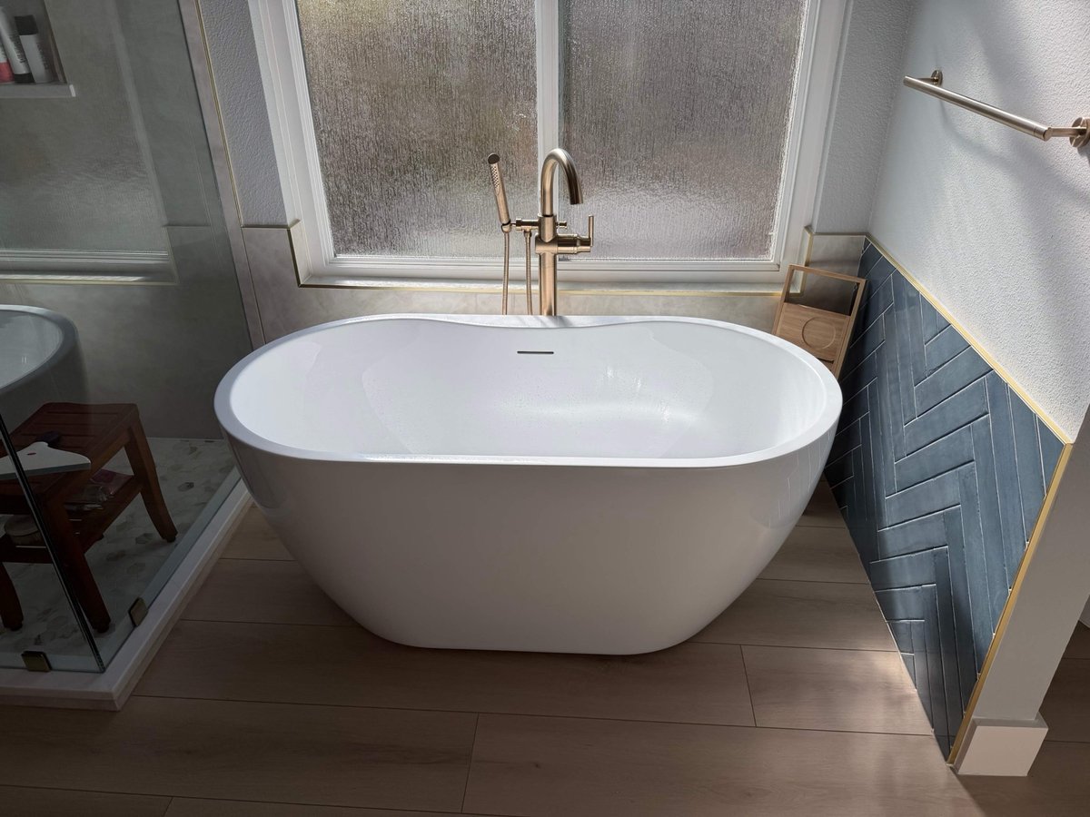 White freestanding tub by frosted window beside blue herringbone tile accent