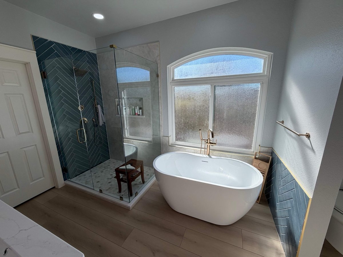 Freestanding tub by arched window next to corner glass shower with blue tile